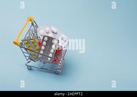 Miniatura carrello della spesa pieno di pillole pastello su fondo azzurro. Foto Stock