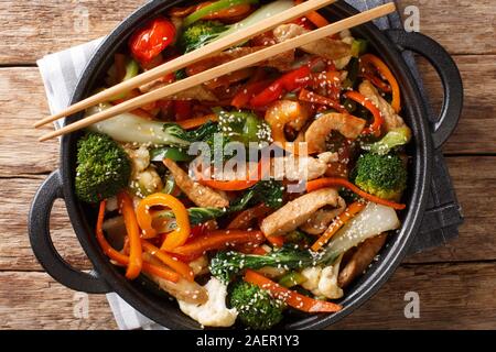 In stile asiatico di maiale fritto con broccoli, cavolo cinese, carote, peperoni, cavolfiore close-up in una padella sul tavolo. Parte superiore orizzontale vista da sopra Foto Stock