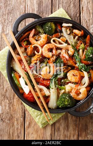 Frutti di mare saltati in padella con verdure fresche di close-up in una padella sul tavolo. Verticale in alto vista da sopra Foto Stock