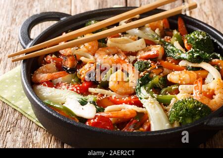 Una pentola mescolare gamberi fritti, calamari e cozze con fresche verdure di stagione di close-up in una padella sul tavolo orizzontale. Foto Stock