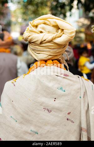 Sadhu indiano in folla andando per rally spirituale. Saggio indiano indossando vestiti arancioni e turbante e tenendo la ghirlanda di fiori Foto Stock