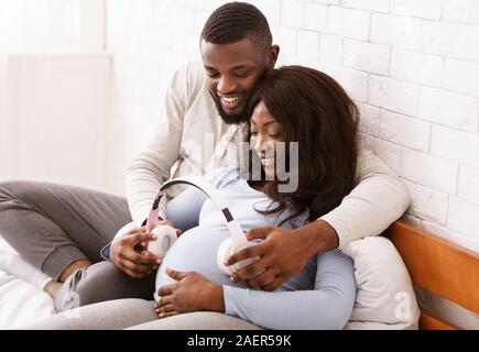 La donna incinta e il marito mettendo le cuffie sul suo ventre Foto Stock