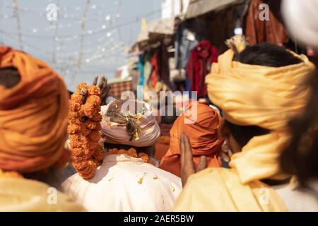 Sadhu indiano in folla andando per rally spirituale. Saggio indiano indossando vestiti arancioni e turbante e tenendo la ghirlanda di fiori Foto Stock