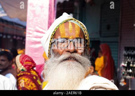 Sadhu indiano in folla andando per rally spirituale. Saggio indiano indossando vestiti arancioni e turbante e tenendo la ghirlanda di fiori Foto Stock