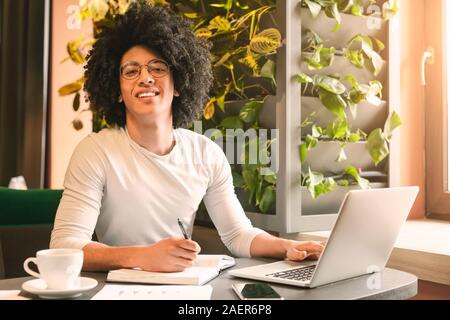 Allegro nero che lavora sul computer portatile e la scrittura del piano strategico Foto Stock