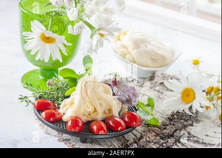 Bianco tradizionale fibroso morbido formaggio di Cecil giace su di una piastra. Il formaggio è decorata con pomodori maturi e uva spina. Foto Stock