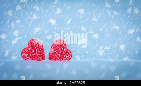 Il giorno di San Valentino Valentine card con due red openwork cuori in un cumulo di neve su uno sfondo blu con la caduta di fiocchi di neve in forma di cuori con co Foto Stock