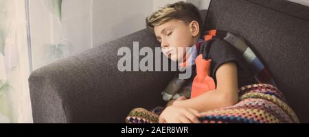 Ragazzo malato a letto con coperta di lana e bottiglie di acqua calda. Triste teen con l'influenza si appoggia a casa da solo in una fredda giornata invernale. Bambino con infettare stagionali Foto Stock