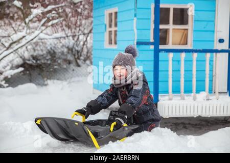 Little Boy slittino in inverno in cantiere. Bambino gode di divertimento invernale. Bambini Un giro in slitta con neve slitta Foto Stock