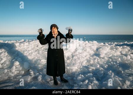 Senior sorridente bella donna in cappotto nero azienda pezzi rotti del mare di ghiaccio in piedi nella parte anteriore del ghiaccio hummocky Foto Stock