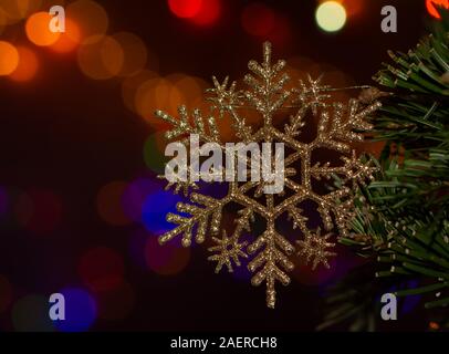 Oro glittery colorate a forma di fiocco di neve ornamento di Natale nella struttura ad albero, con luminosi colorati bokeh sfondo luminoso Foto Stock