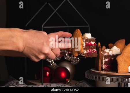Mani femminili tagliare un pezzo di torta Foresta Nera decorata in stile natalizio. Foto Stock
