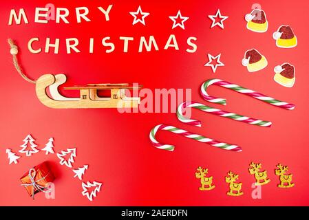 La scritta Buon Natale in legno lettere, giace in piano dal di sopra, isolata su uno sfondo di colore rosso. Visibile candy canes, Natale in legno tre Foto Stock