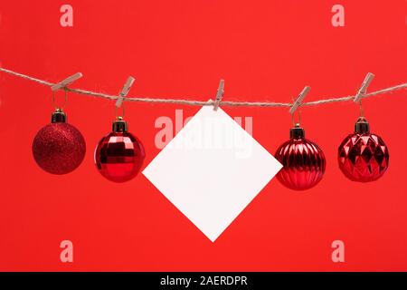 Foglio di carta per appunti clothespins appesi su sfondo rosso con palla di Natale , copia spazio. auguri 2020 Foto Stock