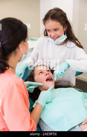 Adorabili bambini dentista in chirurgia dentale con due belle ragazze mostrando loro dental check-up, una ragazza sta giocando assistant Foto Stock