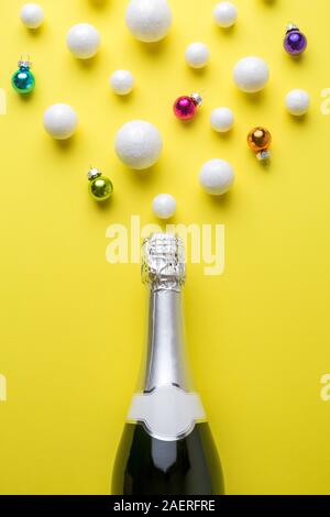 Lay piatto della bottiglia di champagne con bolle fatte di palline di polistirolo e baubles contro sfondo giallo minimo drink creativi concetto. Foto Stock