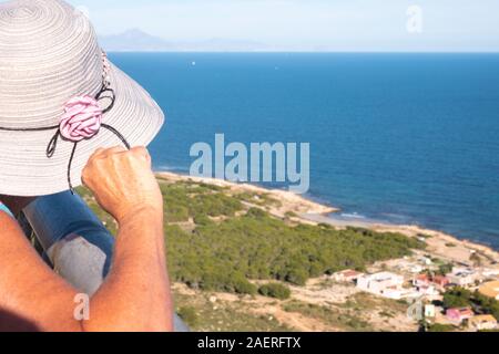 Donna di mezza età che indossa un cappello per il sole guardando la vista dalla Santa Pola Skywalk piattaforma di osservazione sulle scogliere di Partida Bancal de la Arena, Foto Stock