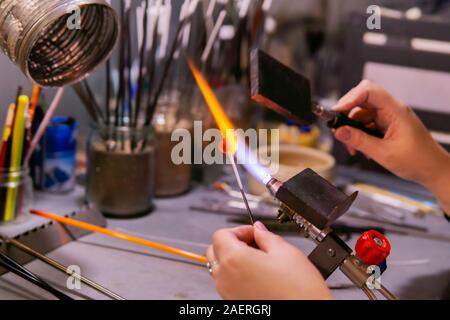 Master con le mani in mano la formazione di un cordone di vetro con una speciale paletta durante beadmaking in un bicchiere da laboratorio di soffiatura Foto Stock