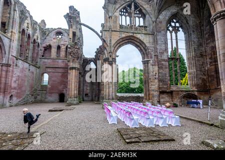 Ragazzo giocando prima di una celebrazione di matrimonio in Melrose Abbey, parzialmente in rovina monastero dell'ordine cistercense in Melrose, Scottish Borders, Scotland, Regno Unito Foto Stock