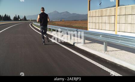 Montare giovane uomo jogging all'aperto sulla strada vuota Foto Stock