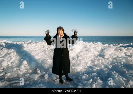 Senior sorridente bella donna in cappotto nero azienda pezzi rotti del mare di ghiaccio in piedi nella parte anteriore del ghiaccio hummocky Foto Stock