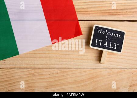 Il messaggio di saluto per il concetto di viaggiatori - Italia Bandiera e lavagna con testo Benvenuti in Italia su sfondo di legno Foto Stock