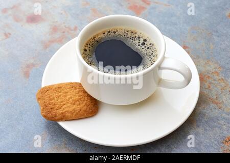 Semplice bianco tazza riempita con caffè nero su bianco piattino con marrone biscotto grigio sul tavolo in metallo con marrone ruggine nella luce morbida Foto Stock