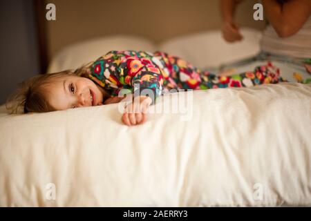 Sorridente ragazza toddler sdraiato sul letto in pigiama. Foto Stock