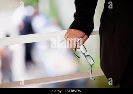 Imprenditrice tenendo un paio di occhiali in mano sorge su un balcone. Foto Stock