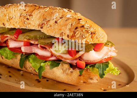 Sandwich con prosciutto, sottaceti, pomodoro fresco e insalata verde su sfondo di legno Foto Stock