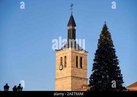 La torre campanaria della chiesa nella Plaza Mayor di Torrejon de Ardoz, accanto a un albero di Natale decorato Foto Stock