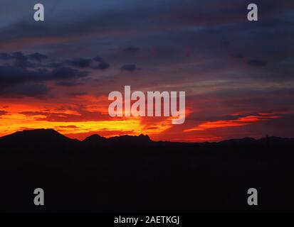 Il sole tramonta dietro un paesaggio montuoso nel deserto di Sonora del sud-ovest Arizona, colata di un pattern a raggiera di calda, fuoco colori dai toni fino Foto Stock