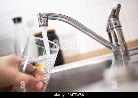 Duesseldorf, Germania. Decimo Dec, 2019. Illustrazione - un uomo tiene un bicchiere sotto l'acqua corrente. Il Bündnis 90/Die Grünen i commenti del gruppo sulla base dei risultati di un'inchiesta sull'acqua nel NRW. Una delle questioni in gioco è lo sviluppo di acqua per uso domestico di consumo. Credito: Marius Becker/dpa/Alamy Live News Foto Stock