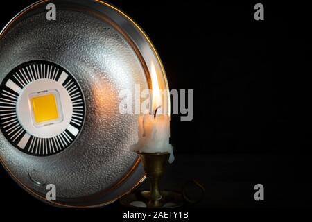 Spento LED luce stroboscopica con riflettore puntando alla candela che brucia sul candelabro vintage, visto in close-up su sfondo nero, misure di paglierino Foto Stock