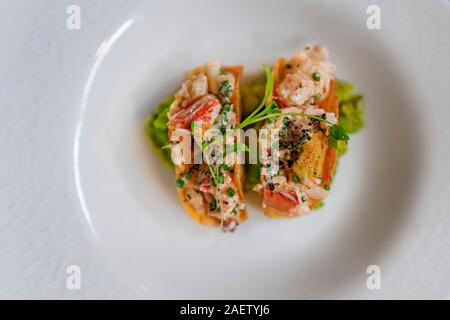 Lobster tacos dorados su di una piastra in un ristorante di lusso, servito con germogli di coriandolo e purea di avocado in hard croccante tortilla di mais conchiglie, laici piatta Foto Stock