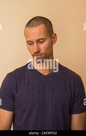 Ritratto di un meditabondo giovane uomo in blu o porpora photoball contro un muro beige. Foto Stock