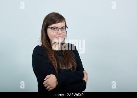 Sorridente giovane donna in abiti casual tenendo le mani incrociate, abbracciando se stessa Foto Stock