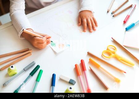 Chiusura del bambino con le mani in mano disegno nel libro bianco all'interno colorato Matite e penne. Foto Stock