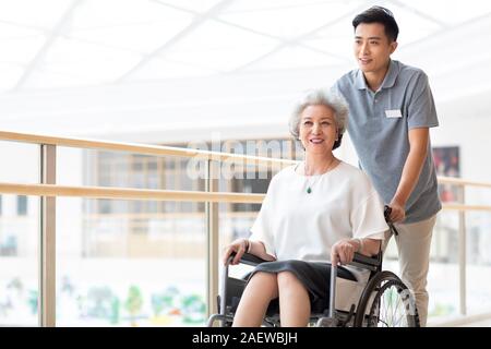 Assistente infermieristica avendo cura di senior donna in sedia a rotelle Foto Stock