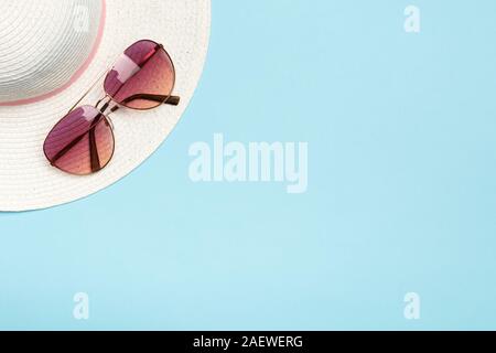Rosa occhiali da sole e un cappello bianco su sfondo blu. Il concetto di estate, viaggi, vacanze e mare. Foto Stock