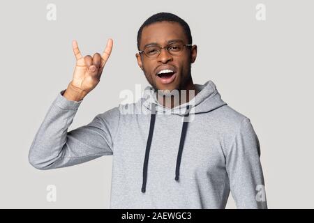 Giocoso eccitato giovane americano africano guy cantando, mostrando le corna segno. Foto Stock