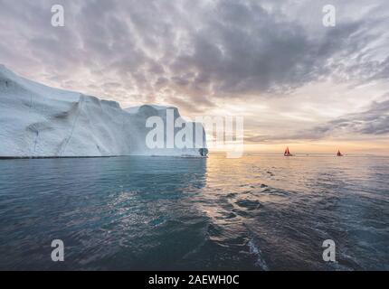 Bella rossa di barca a vela in artico accanto a un enorme iceberg che mostra la scala. Navigando tra iceberg galleggianti nella baia di Disko glacier durante Foto Stock