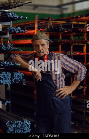 Ritratto di coppia meccanico tute in piedi vicino a tubi di metallo e guardando la telecamera in magazzino Foto Stock