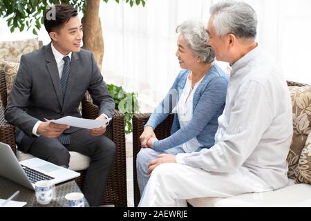 Felice coppia senior a parlare con il consulente finanziario in salotto Foto Stock