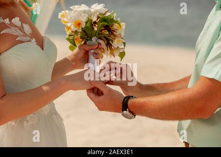 Primo piano di una giovane scambiare gli anelli di nozze nel corso di una cerimonia di matrimonio sulla spiaggia. Matrimonio e luna di miele concetto. Foto Stock