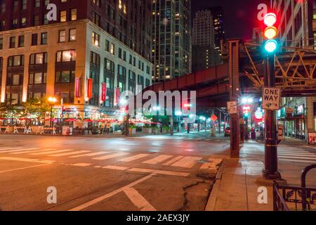 Chicago, IL - Circa 2019: notte lungo tempo di esposizione del centro occupato intersezione sotto loop binari del treno con il traffico spia di controllo accesa verde giallo r Foto Stock