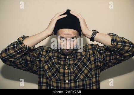 Giovane uomo, modello di moda, indossando un plaid shirt con un cieco biege dietro di lui. Guy in black hat con la barba in stile casual. Foto Stock