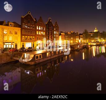Splendida e tranquilla vista notturna della città di Amsterdam. Di notte le luminarie di stile olandese edifici con riflessioni su acqua e barche nel canale. Nethe Foto Stock