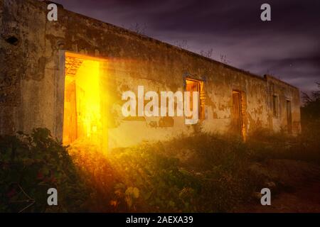 Colorato night shot di una vecchia casa abbandonata con misteriosi calda luce splendente fuori dall'ingresso Foto Stock