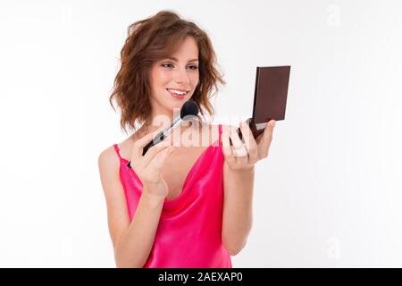 Giovane bella ragazza fare il trucco con specchio piccolo isolato su sfondo bianco Foto Stock